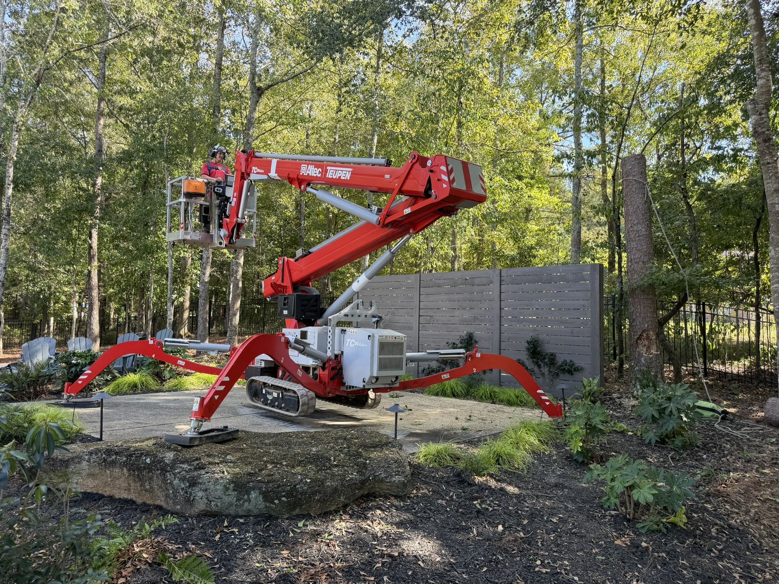 Tracked aerial lift set up on a stone patio in a landscaped garden